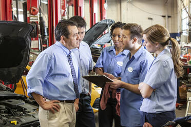 Ein Team von Mechanikern, die an einem Auto arbeiten, diskutiert ein Problem in einer Autowerkstatt - MINF15894