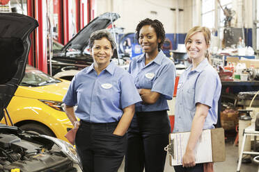 Porträt von drei lächelnden Mechanikerinnen in einer Autowerkstatt - MINF15895