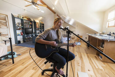 Vierzehnjähriges Teenager-Mädchen spielt Gitarre und singt zu Hause auf dem Dachboden - MINF15916