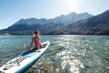 Germany, Bavaria, Garmisch Partenkirchen, Young woman sitting on stand up paddle board on Lake Eibsee and lookingat Zugspitze Mountain - WFF00481