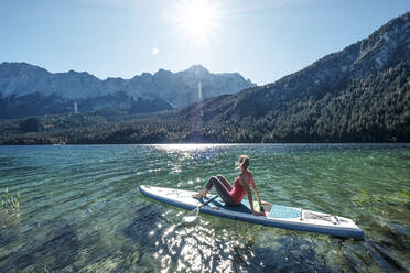 Deutschland, Bayern, Garmisch Partenkirchen, Junge Frau sitzt auf einem Stand Up Paddle Board auf dem Eibsee und schaut auf die Zugspitze - WFF00482