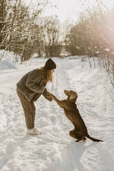 Teenage girl playing with dog in snow at winter dawn - OJF00426