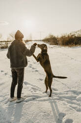 Teenage girl playing with dog in snow at winter sunrise - OJF00427