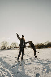 Teenage girl playing with dog in snow at winter dawn - OJF00428