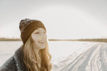 Porträt eines schönen Teenagers, der im Freien steht und gegen die aufgehende Wintersonne lächelt - OJF00433