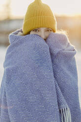 Porträt eines schönen Mädchens mit Strickmütze, das sich an einer Wolldecke wärmt - OJF00439