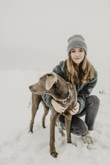 Porträt eines Mädchens im Teenageralter, das im Schnee hockt und einen Labrador Retriever umarmt - OJF00442