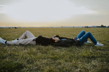 Male friends lying down on grass in park during sunset - MASF22055