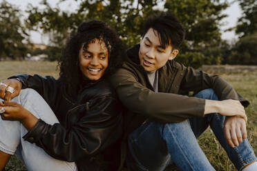 Happy friends sitting side by side in park during sunset - MASF22056