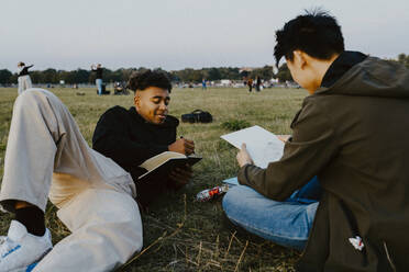 Männliche Freunde zeichnen in einem Buch im Park während des Sonnenuntergangs - MASF22062