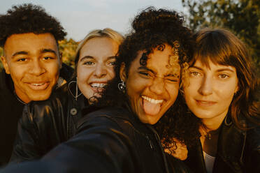 Cheerful friends taking selfie outdoors during sunset - MASF22075