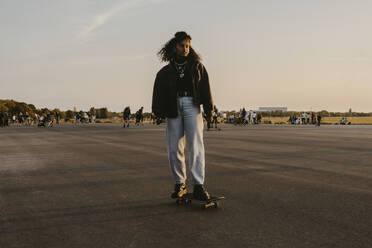 Young woman standing on skateboard against sky in park - MASF22078