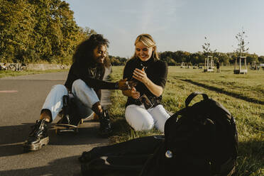 Lächelnde Freundinnen mit Smartphone im Park sitzend - MASF22101