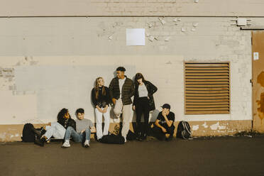 Junge Freunde verbringen ihre Freizeit auf einem Gehweg an einer Mauer - MASF22108