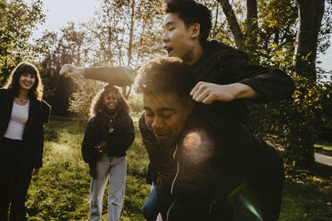 Young man carrying piggyback to male friend in park - MASF22119