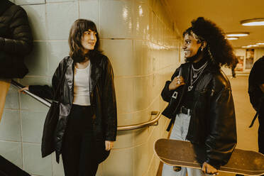 Smiling female friends looking at each other in illuminated subway - MASF22129