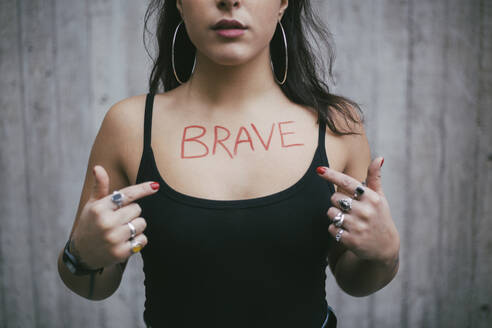 Midsection of female protestor pointing on brave text written over chest against wall - MASF22141