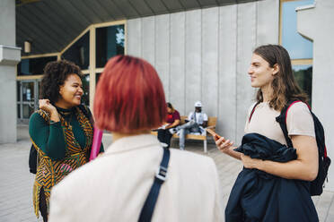 Happy university students talking while standing in college campus - MASF22271