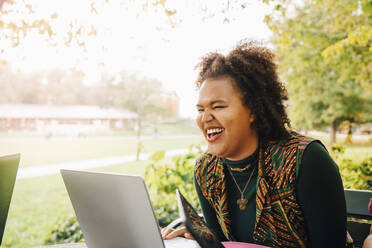 Lachende Studentin beim Online-Studium mit Laptop auf dem College-Campus - MASF22275