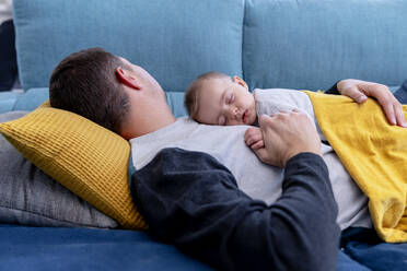 Father sleeping with baby boy on sofa at home - AMPF00094