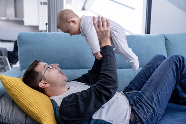 Verspielter Vater mit einem kleinen Jungen, der zu Hause auf dem Sofa liegt - AMPF00098