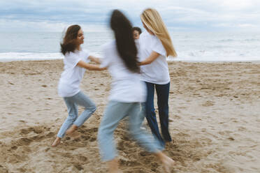 Young female friends running in circle while playing at beach during vacations - ARTF00010