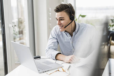 Young male professional attending video call through laptop sitting at desk - UUF22836