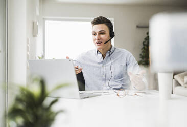 Young businessman gesturing while attending video call on laptop in home office - UUF22837