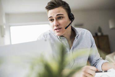 Young male professional discussing on video call through laptop in home office - UUF22839