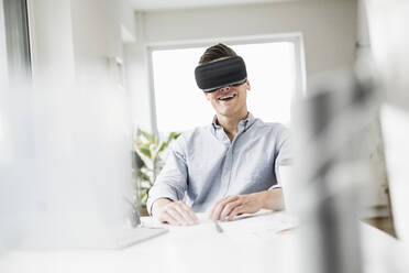 Male entrepreneur wearing virtual reality simulator while sitting at desk - UUF22841