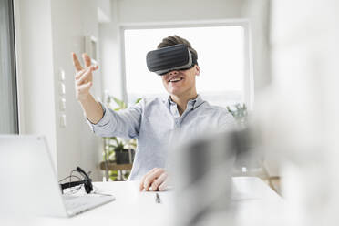 Young businessman gesturing while wearing virtual reality simulator at home office - UUF22843