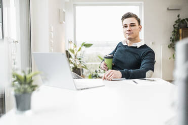 Geschäftsmann mit Einweg-Kaffeebecher im Büro zu Hause sitzend - UUF22849