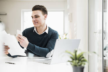 Männlicher Unternehmer hält ein Dokument und benutzt ein Smartphone - UUF22853