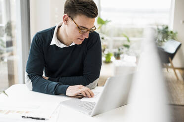 Businessman wearing eyeglasses reading document while sitting at desk - UUF22866