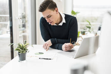 Concentrated male professional reading document while sitting in home office - UUF22868