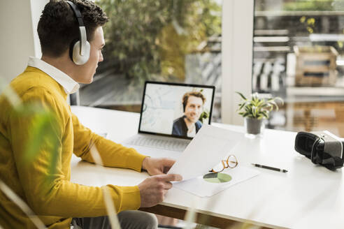Businessman explaining document while attending business meeting through video conference at home office - UUF22875
