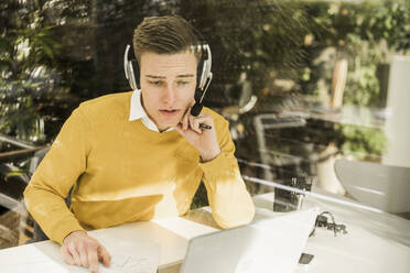 Young male professional wearing headphones attending business meeting in home office - UUF22879