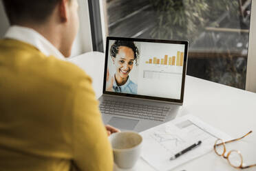 Businessman discussing through video conference while sitting at desk in home office - UUF22890