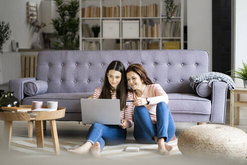 Smiling mother holding credit card while daughter paying bills through laptop at home - GIOF11452