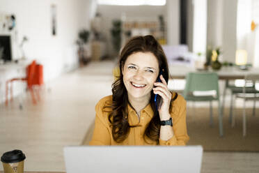 Smiling businesswoman looking away while talking on mobile phone at home office - GIOF11466