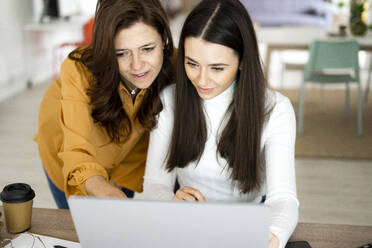 Mother assisting daughter while studying on laptop at home - GIOF11477