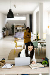 Young woman with book studying at table in living room - GIOF11479