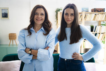 Lächelnde Geschäftsfrau und Tochter stehen im Wohnzimmer - GIOF11504