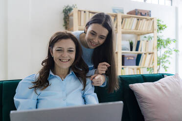 Eine lächelnde Geschäftsfrau und ihre Tochter schauen auf einen Laptop im Heimbüro - GIOF11515