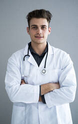 Männlicher gut aussehender Arzt mit verschränkten Armen vor einer grauen Wand - GIOF11521
