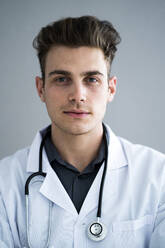 Handsome male doctor against gray wall in hospital - GIOF11522