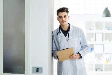 Männlicher Arzt mit Klemmbrett an die Wand gelehnt im Krankenhaus - GIOF11528