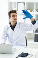 Konzentrierter männlicher Wissenschaftler, der eine Flüssigkeit im Reagenzglas untersucht, während er einen Laptop im Labor benutzt - GIOF11532