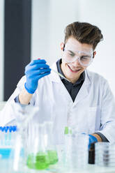 Lächelnder männlicher Wissenschaftler, der bei der Arbeit im Labor eine Pipette hält - GIOF11539