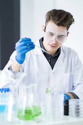 Konzentrierter männlicher Wissenschaftler mit Schutzbrille bei der Arbeit im Labor - GIOF11540